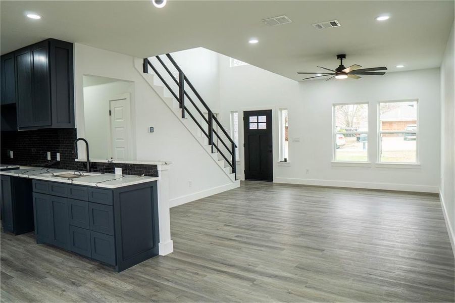 Kitchen with ceiling fan, backsplash, light stone counters, and light hardwood / wood-style flooring