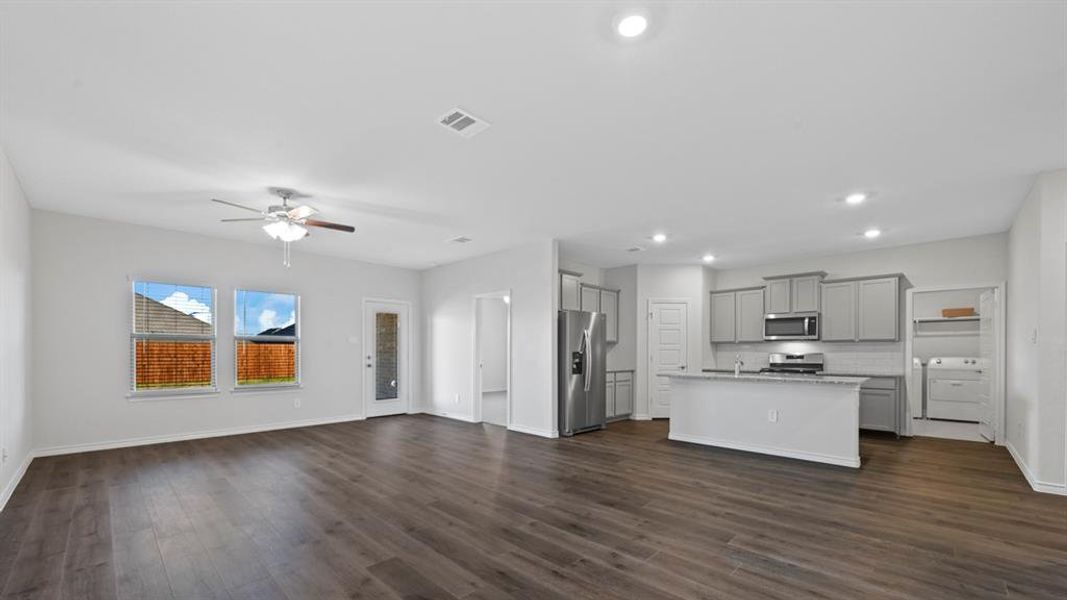 Kitchen featuring gray cabinets, open floor plan, appliances with stainless steel finishes, a center island with sink, and washer / clothes dryer Kitchen featuring gray cabinets, open floor plan, appliances with stainless steel finishes, a center island with sink, and washer / clothes dryer
