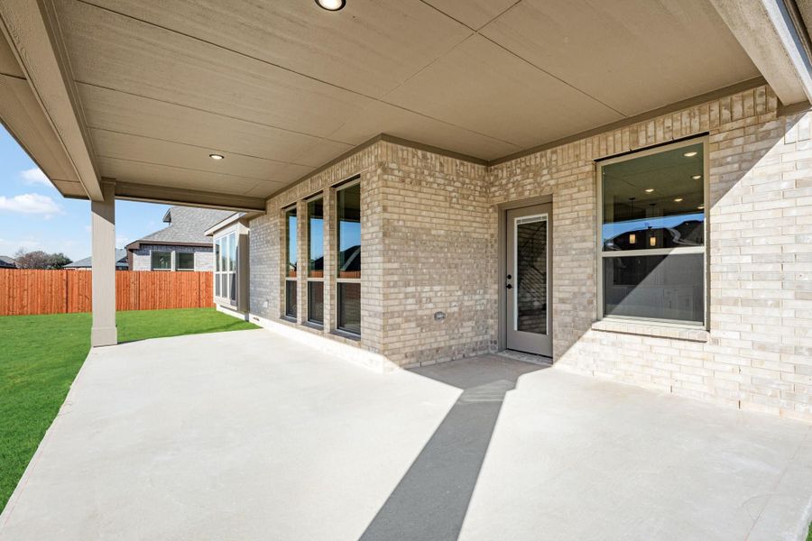 Covered back patio with concrete slab, brick exterior, and fenced backyard with green lawn