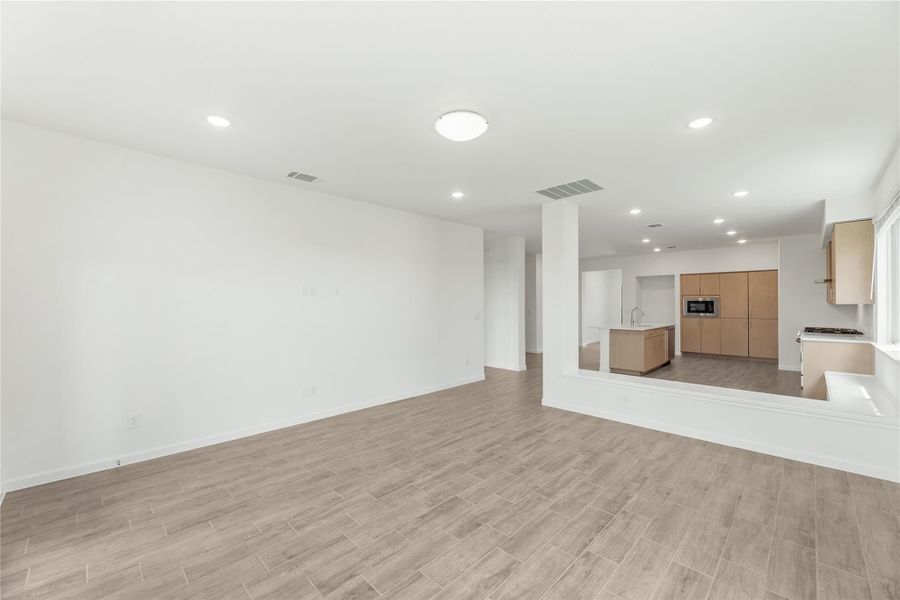 Open living area with wood-look tile floors leading to a modern kitchen with tan cabinets and center island