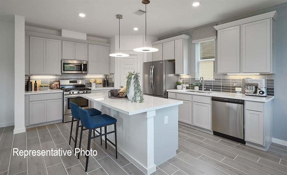 Modern kitchen featuring a large central island with countertop seating, light-toned cabinetry, stainless steel appliances, and wood-finish flooring