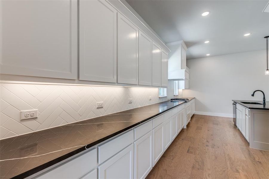 Kitchen featuring white cabinetry, decorative backsplash, pendant lighting, light wood-type flooring, and sink