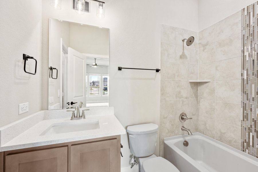 Bathroom with quartz vanity, tiled shower-tub combo, and mosaic accent tile wall