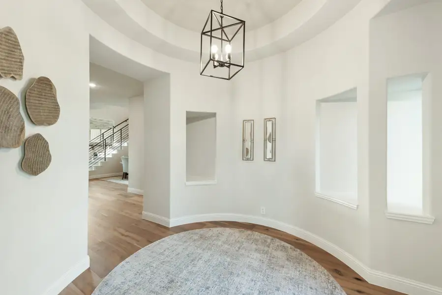 Curved foyer with round tray ceiling, geometric pendant light, hardwood floors, and staircase view