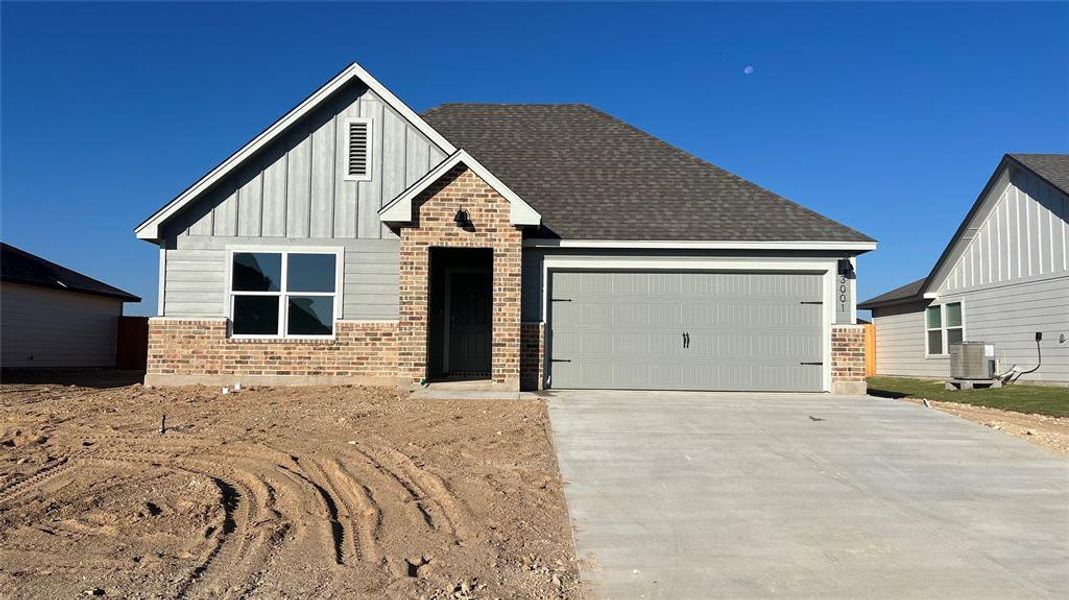 View of front of home featuring brick siding, board and batten siding, concrete driveway, an attached garage, and roof with shingles