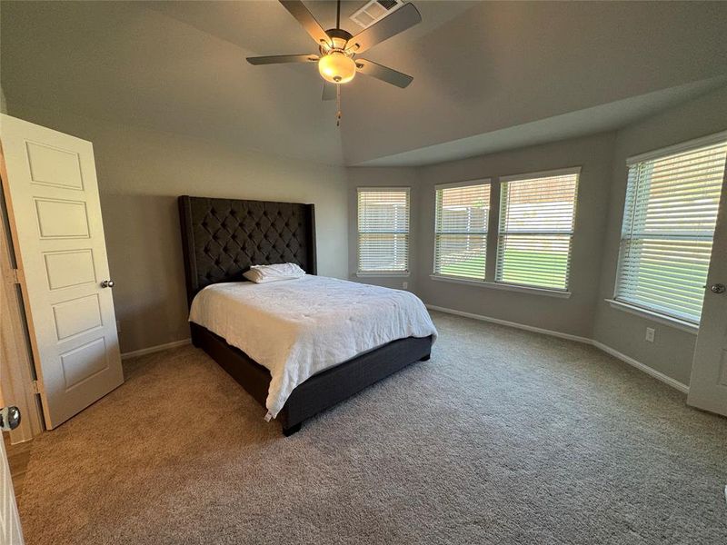Carpeted bedroom featuring a vaulted ceiling with a ceiling fan, a bay window with multiple panes, and paneled doors Carpeted bedroom featuring a vaulted ceiling with a ceiling fan, a bay window with multiple panes, and paneled doors
