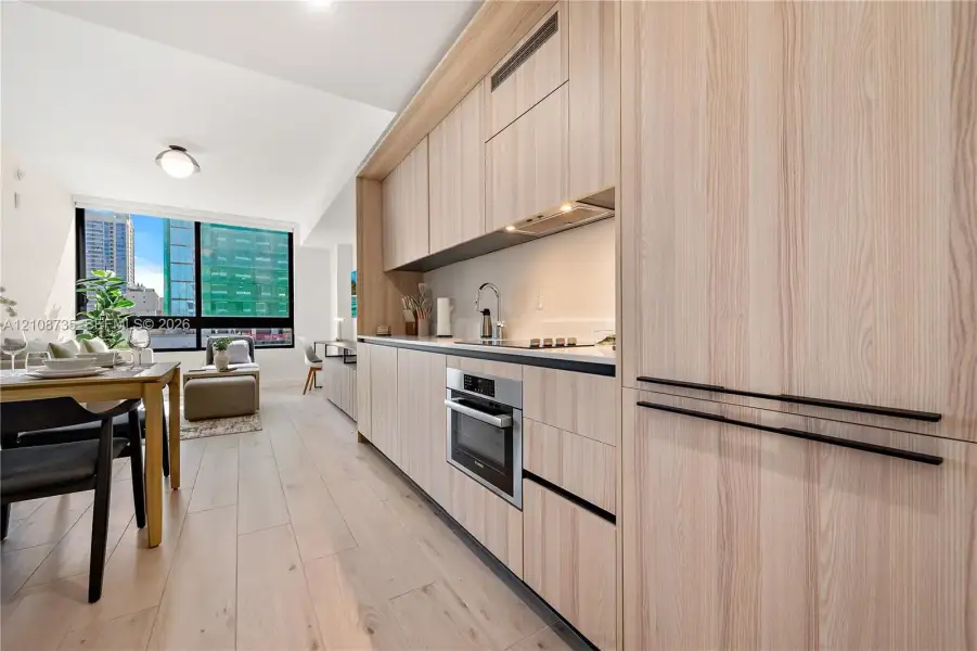 Kitchen featuring wood-finish cabinetry with matte black pulls, integrated stainless steel appliances, a light-toned countertop, and wood-finish flooring throughout Kitchen featuring wood-finish cabinetry with matte black pulls, integrated stainless steel appliances, a light-toned countertop, and wood-finish flooring throughout