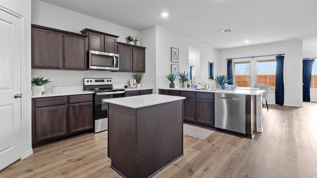 Kitchen featuring a peninsula, stainless steel appliances, dark wood finish cabinetry, a kitchen island, and light wood-style floors Kitchen featuring a peninsula, stainless steel appliances, dark wood finish cabinetry, a kitchen island, and light wood-style floors