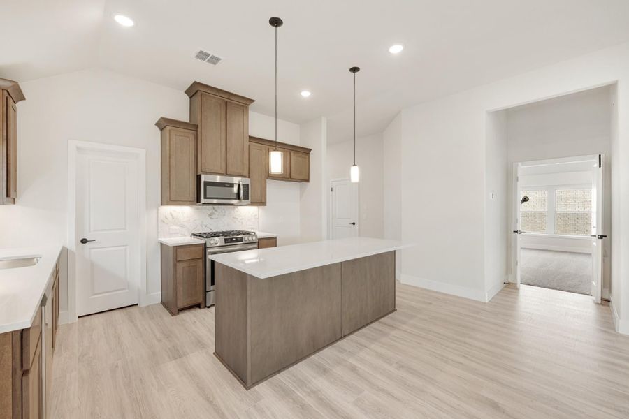 Kitchen with brown cabinets, center island, stainless steel appliances, and light wood floors