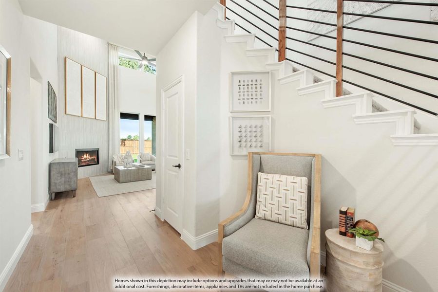 Entryway with white staircase, hardwood floors, and view into living room with fireplace and high ceilings