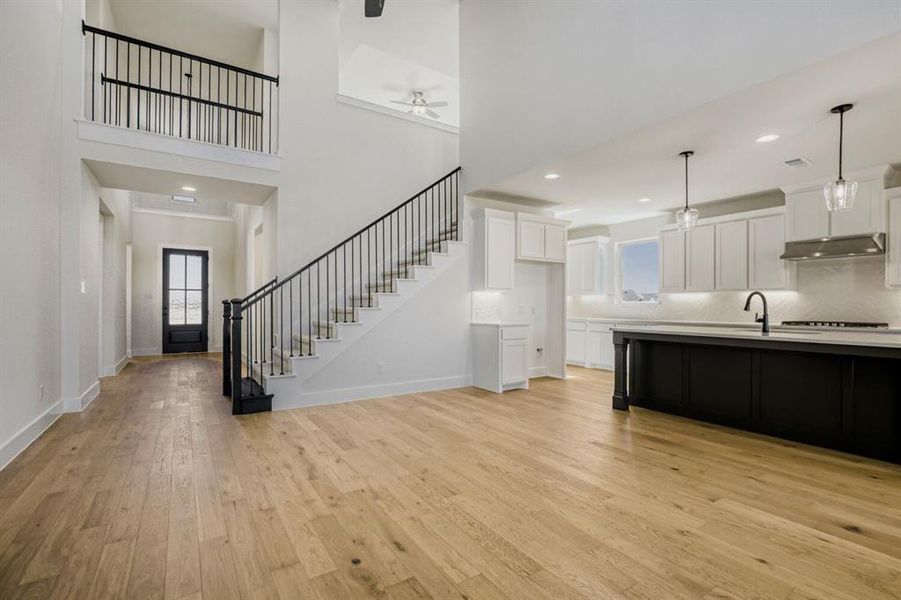 Two tone kitchen featuring ceiling fan, pendant lighting, a high ceiling, light wood finished floors, and dual tone cabinets