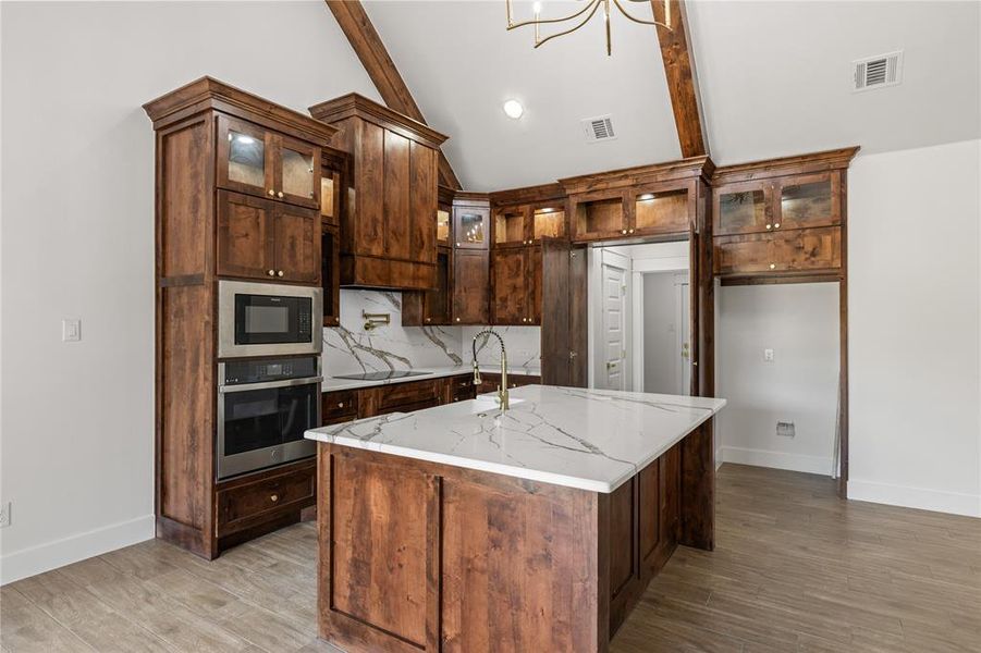 Kitchen featuring glass insert cabinets, stainless steel appliances, tasteful backsplash, light wood finished floors, and light stone counters