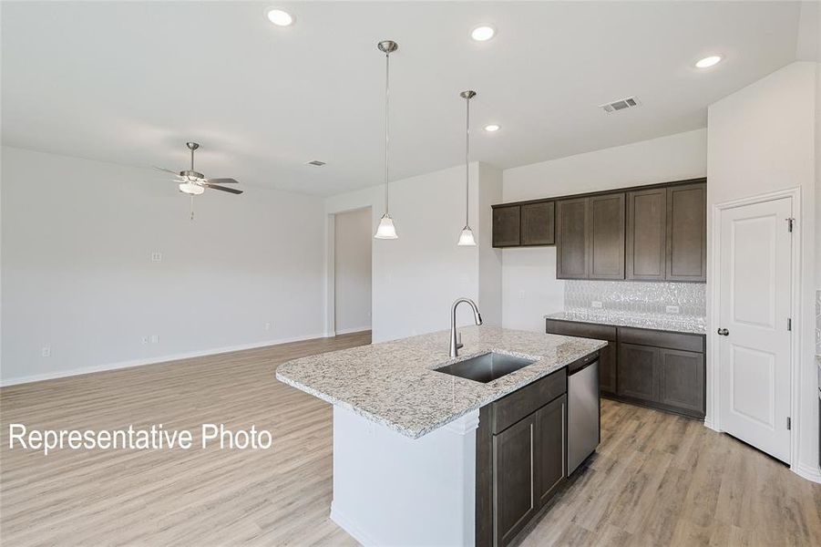 Kitchen featuring ceiling fan, decorative backsplash, light hardwood / wood-style flooring, sink, and a center island with sink