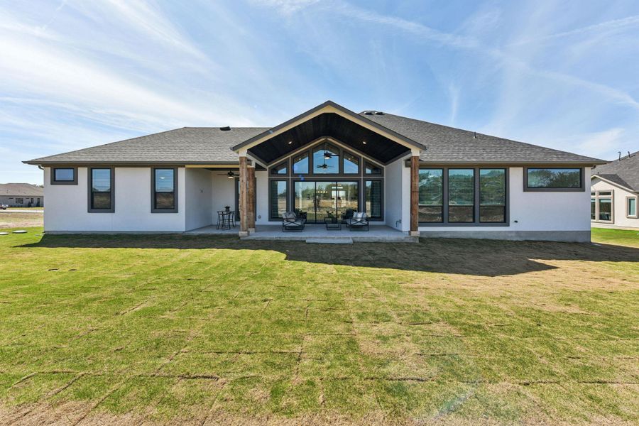Rear view of house with a lawn, a patio, stucco siding, and a shingled roof