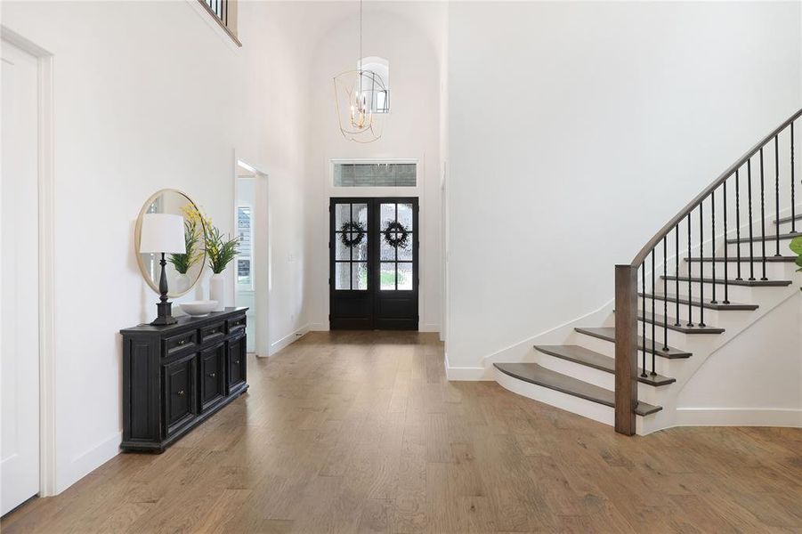Grand entryway featuring vaulted ceilings, wood-finish flooring, a curved staircase with wrought iron balusters, and double entry doors with transom windows