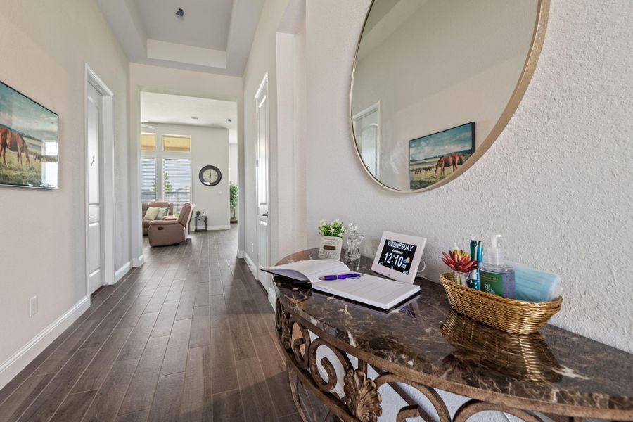 This inviting wide entry way hallway features elegant dark wood tile flooring and a decorative console with a mirror. It leads to a cozy living area filled with natural light from large windows. The space is well-organized and welcoming, ideal for a warm home atmosphere. This inviting wide entry way hallway features elegant dark wood tile flooring and a decorative console with a mirror. It leads to a cozy living area filled with natural light from large windows. The space is well-organized and welcoming, ideal for a warm home atmosphere.