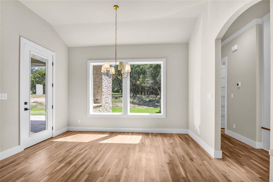 Unfurnished dining area with arched walkways, light wood-type flooring, a chandelier, and lofted ceiling