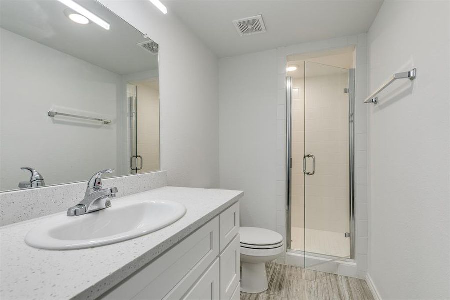 Bathroom with hardwood / wood-style floors, vanity, toilet, and an enclosed shower