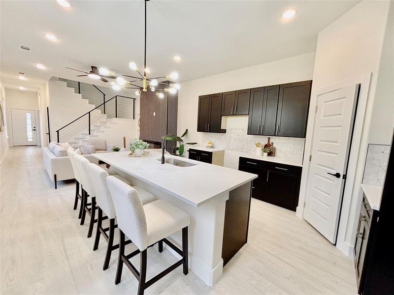 Kitchen with a breakfast bar area, an island with sink, hanging lights, light wood-style floors, and light stone countertops