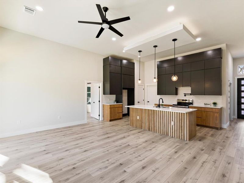 Kitchen featuring modern cabinets, hanging light fixtures, a kitchen island with sink, a ceiling fan, and stainless steel range with electric stovetop