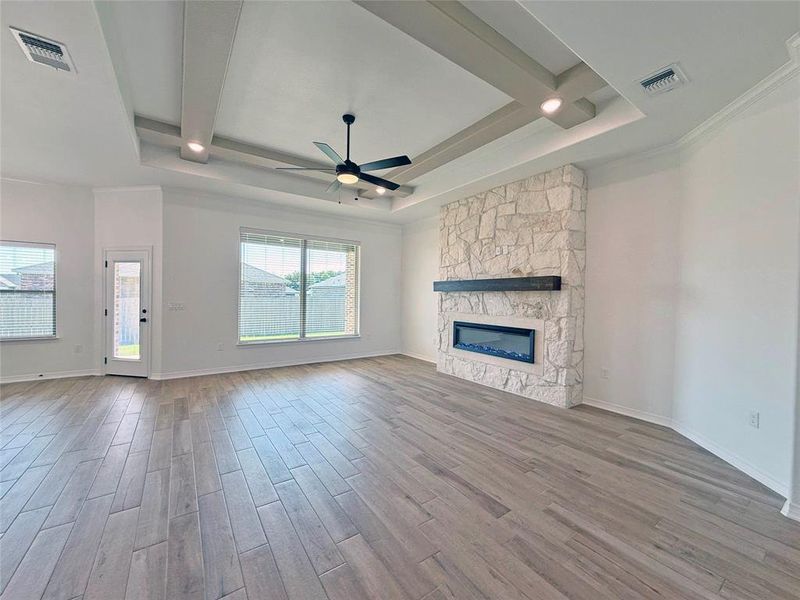 Unfurnished living room with light wood finished floors, a ceiling fan, a fireplace, and a tray ceiling