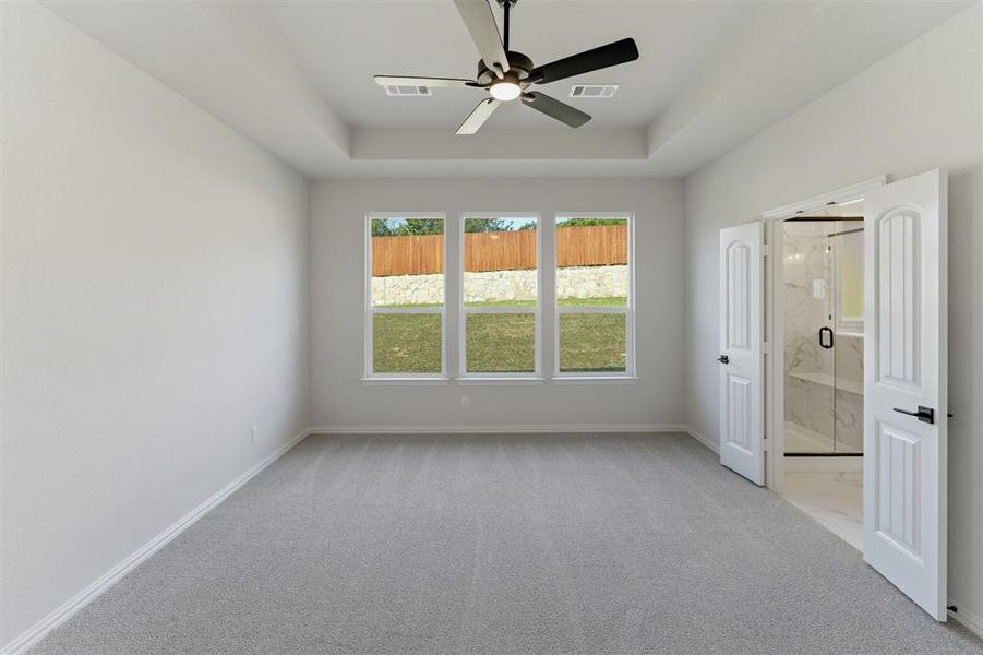 Unfurnished bedroom featuring light colored carpet, a ceiling fan, a tray ceiling, and ensuite bathroom