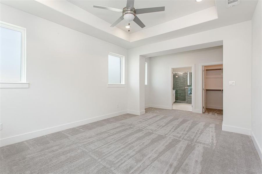 Empty room featuring a tray ceiling, ceiling fan, and light colored carpet