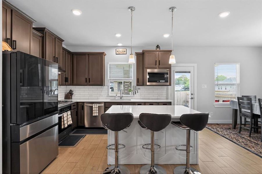 Kitchen featuring dark wood cabinetry, stainless steel appliances, a white subway tile backsplash, and a central island with pendant lighting