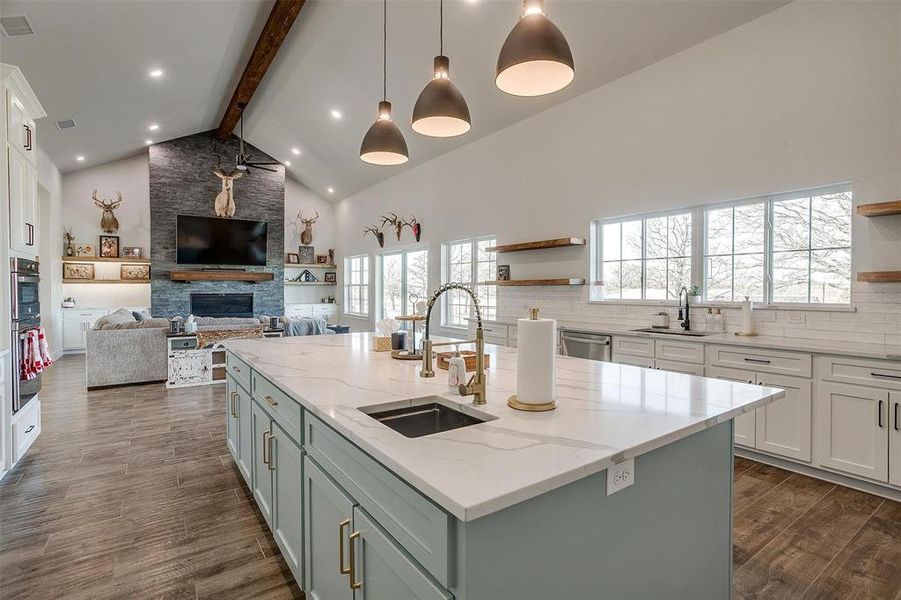 Kitchen featuring sink, hanging light fixtures, an island with sink, beamed ceiling, and light stone countertops