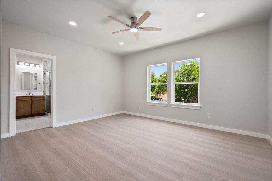 An airy bedroom with wood flooring and a view of the vibrant trees outside.