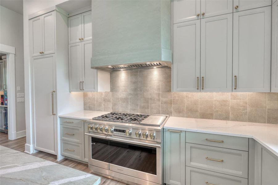 Kitchen with stainless steel range, custom exhaust hood, light wood-style floors, and decorative backsplash