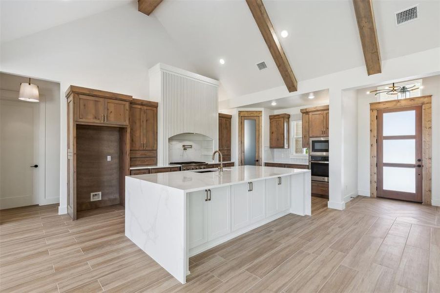 Kitchen with beam ceiling, decorative backsplash, a center island with sink, and stainless steel appliances