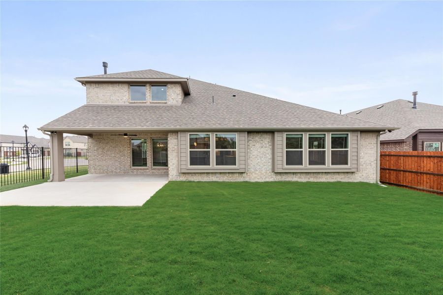 Rear exterior of brick home with covered patio, large windows, and green backyard lawn Rear exterior of brick home with covered patio, large windows, and green backyard lawn
