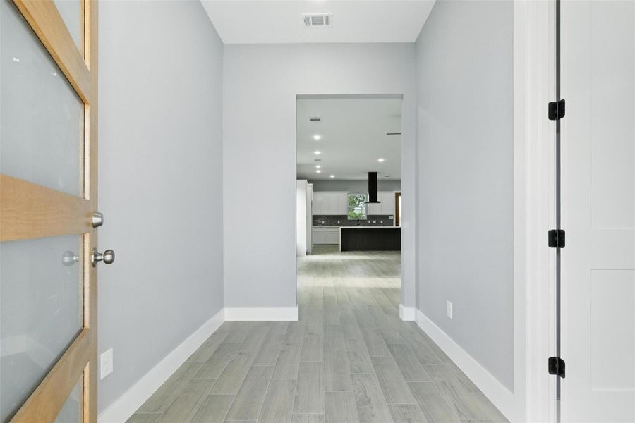 This photo showcases a modern, inviting entryway leading to an open-concept kitchen. It features sleek gray walls, light flooring, and ample lighting, creating a bright and welcoming atmosphere.