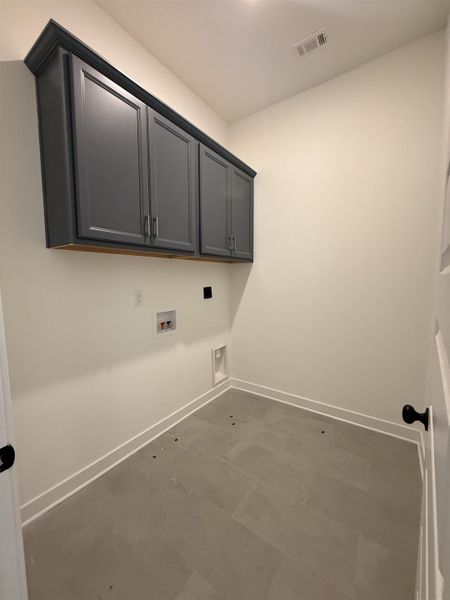 Utility area featuring gray shaker cabinetry with crown molding, light gray tile flooring, and white baseboard trim