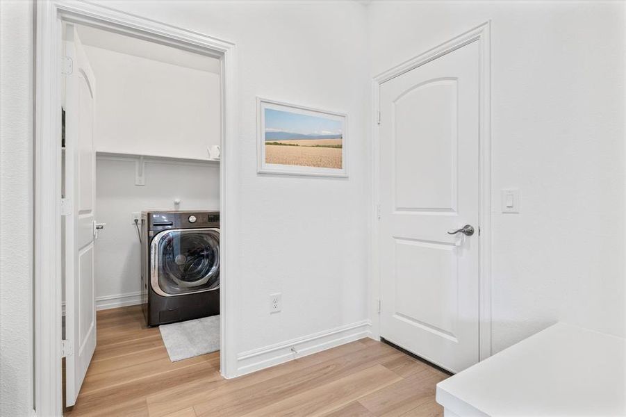 Dedicated laundry area featuring a front-load washer, wood-finish flooring, and crisp white trim