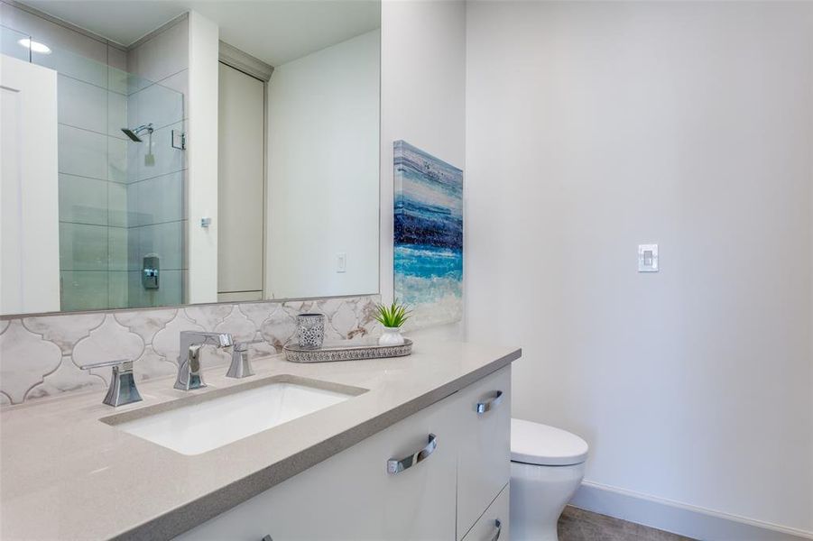 Bathroom featuring tiled shower, vanity, decorative backsplash, and toilet