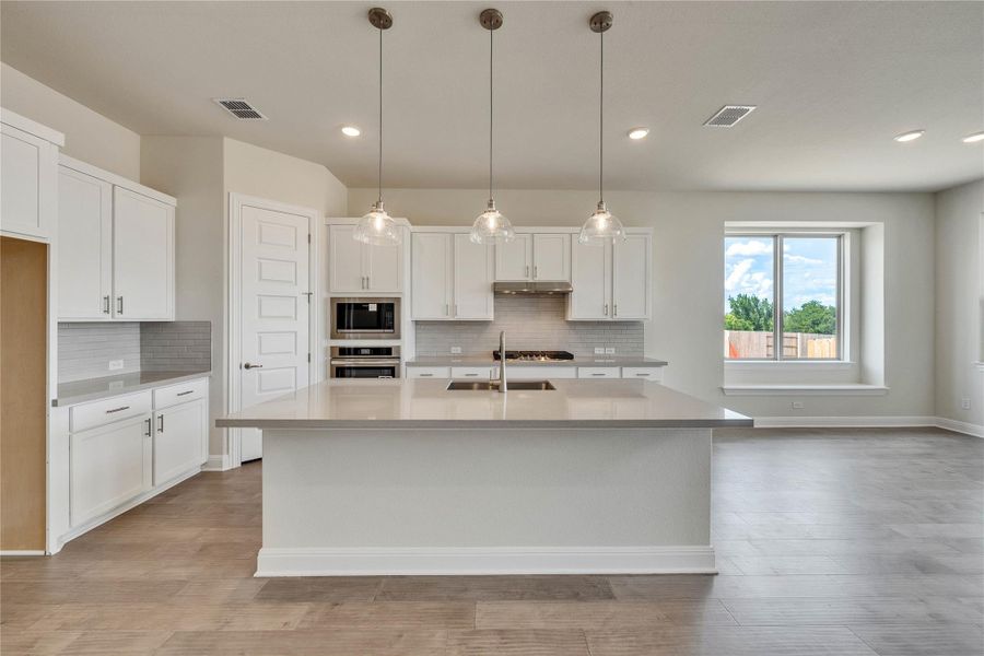 Kitchen featuring backsplash, light countertops, light wood-type flooring, white cabinets, and stainless steel oven Kitchen featuring backsplash, light countertops, light wood-type flooring, white cabinets, and stainless steel oven