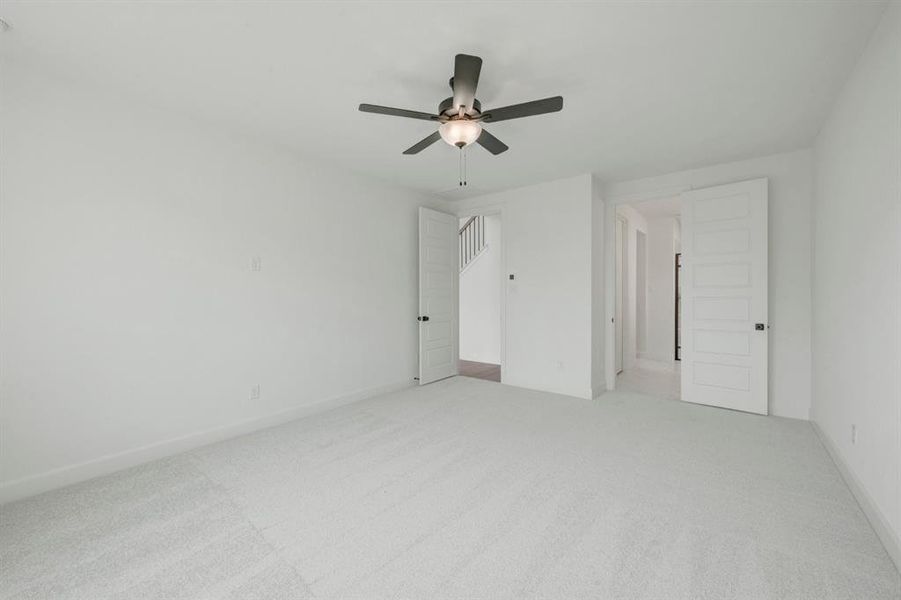 Spacious room featuring light-colored carpeting, white walls, and a ceiling fan with integrated lighting
