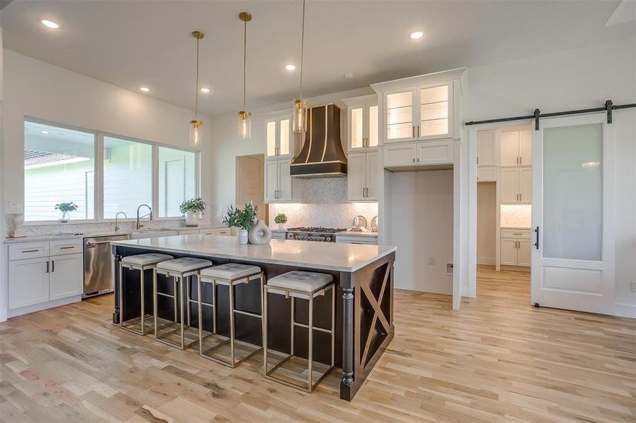 Kitchen with white cabinets, decorative light fixtures, custom range hood, a center island, and a barn door