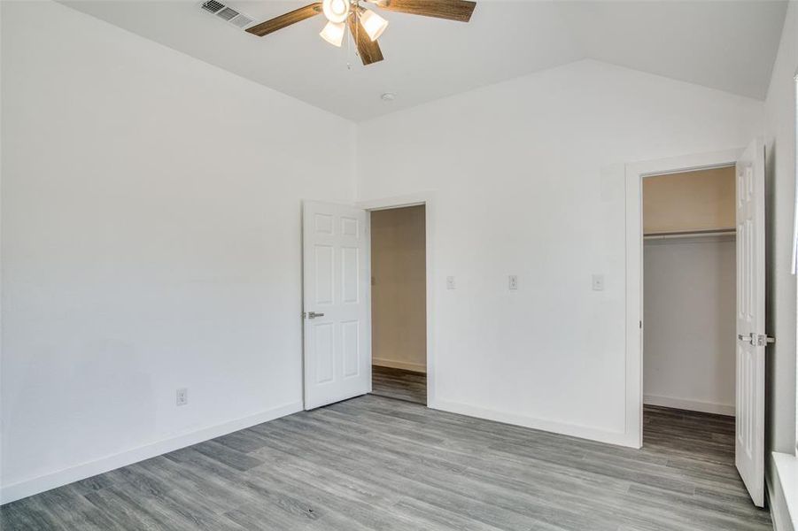 Unfurnished bedroom with wood-type flooring, a closet, vaulted ceiling, ceiling fan, and a walk in closet Unfurnished bedroom with wood-type flooring, a closet, vaulted ceiling, ceiling fan, and a walk in closet
