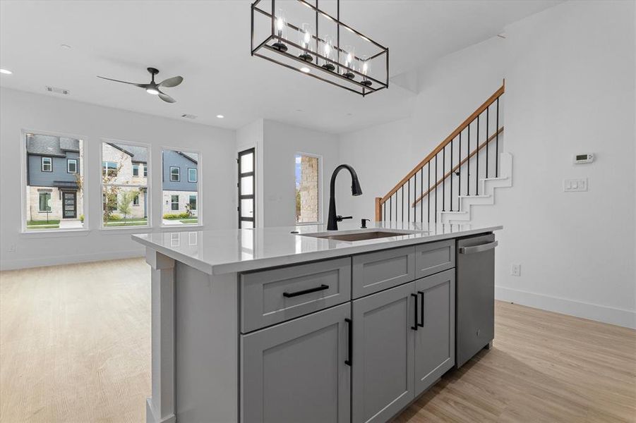Kitchen with gray cabinetry, a kitchen island with sink, light stone countertops, stainless steel dishwasher, and hanging light fixtures Kitchen with gray cabinetry, a kitchen island with sink, light stone countertops, stainless steel dishwasher, and hanging light fixtures