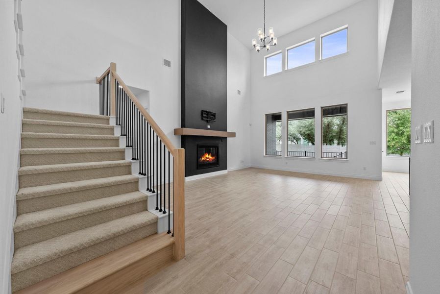 Bright and open living area with soaring ceilings, a dramatic black accent fireplace, and a striking staircase with wood and iron detailing.