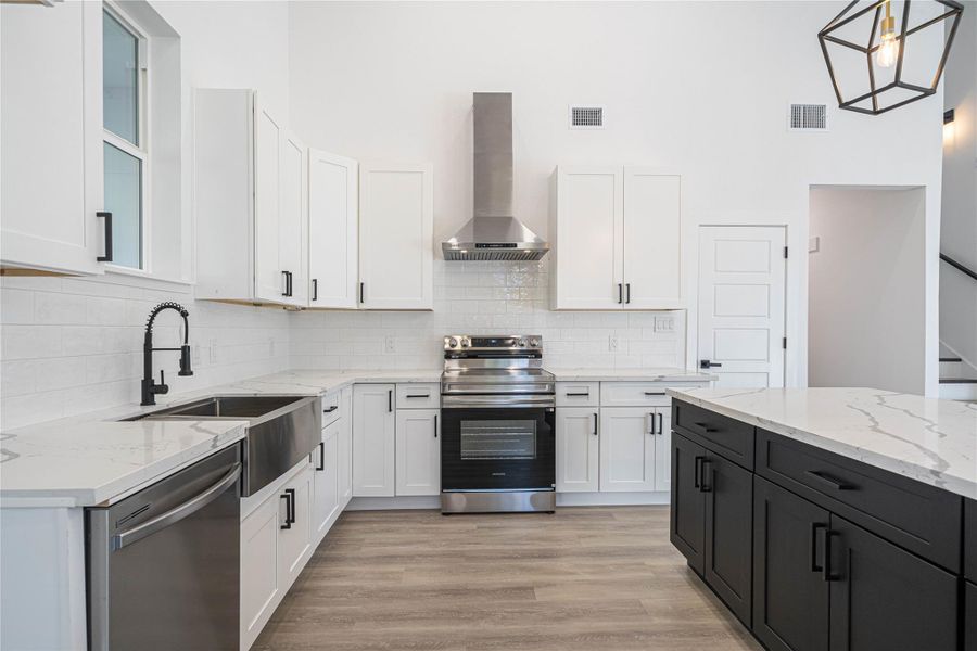 Kitchen featuring light stone counters, white cabinets, stainless steel appliances, wall chimney exhaust hood, and light wood-type flooring