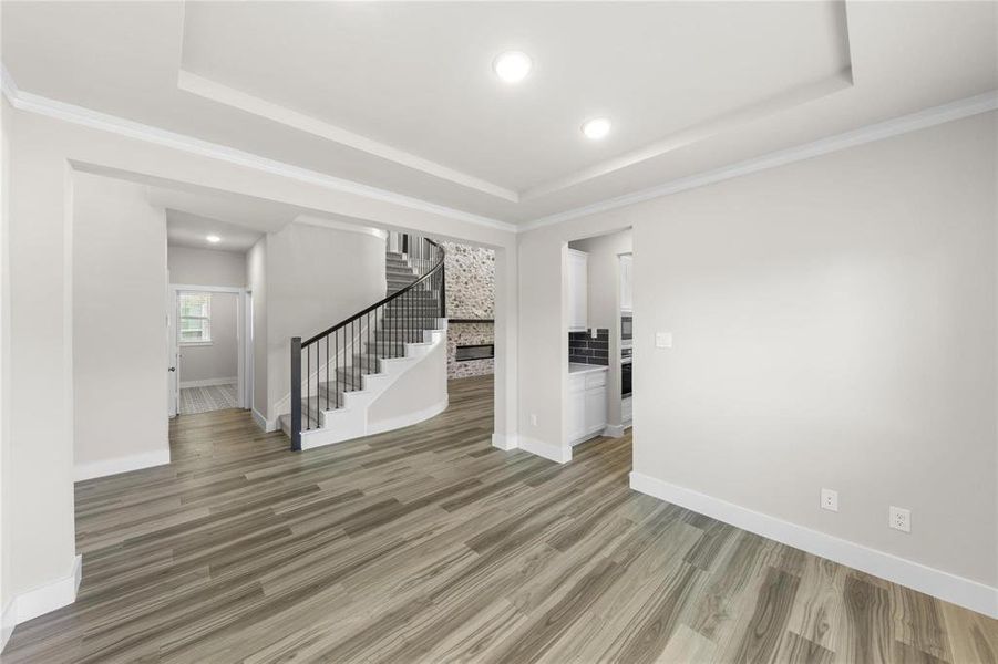 Spacious interior showcasing wood-finish flooring, a contemporary curved staircase with wrought iron balusters, recessed lighting, and tray ceilings Spacious interior showcasing wood-finish flooring, a contemporary curved staircase with wrought iron balusters, recessed lighting, and tray ceilings