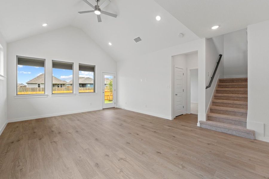 A naturally illuminated living space features vaulted ceilings and light wood flooring, with a stairway leading to the next level. A naturally illuminated living space features vaulted ceilings and light wood flooring, with a stairway leading to the next level.