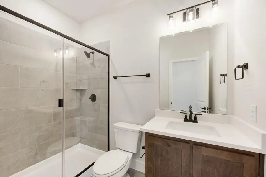 Bathroom with wood vanity, white countertop, glass shower with gray tile, and black fixtures