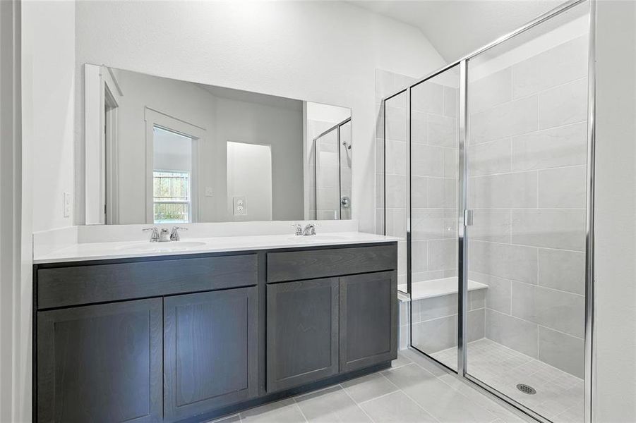 Bathroom featuring a stall shower, double vanity, vaulted ceiling, and tile patterned flooring