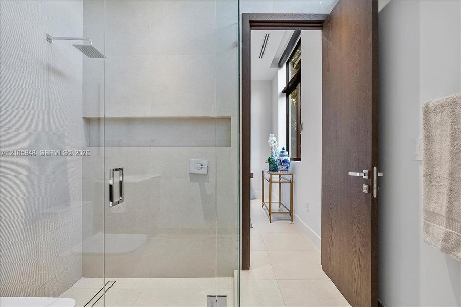 Walk-in shower featuring glass enclosure, wall-mounted rainfall showerhead, and integrated recessed shelving, complemented by a solid wood-finish door with brushed metal hardware