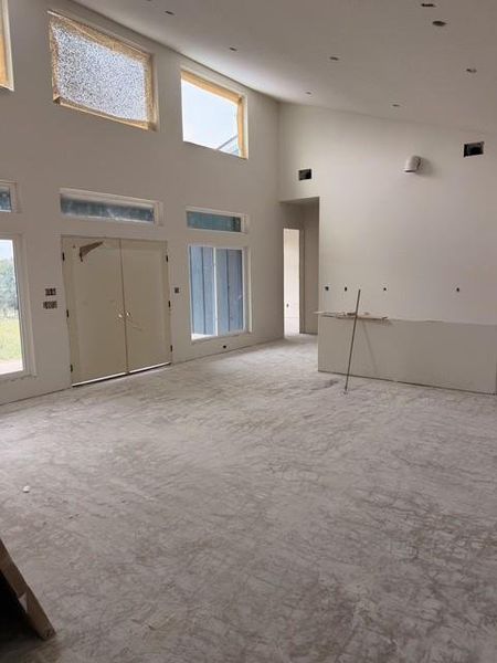 Spacious interior featuring a high vaulted ceiling, multiple windows, double entry doors, recessed ceiling lighting, and a partial wall structure